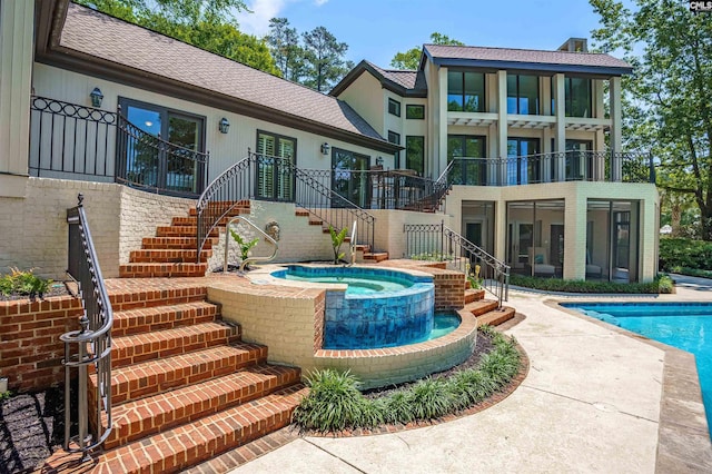 rear view of house with stairs, a shingled roof, an in ground hot tub, and an outdoor pool