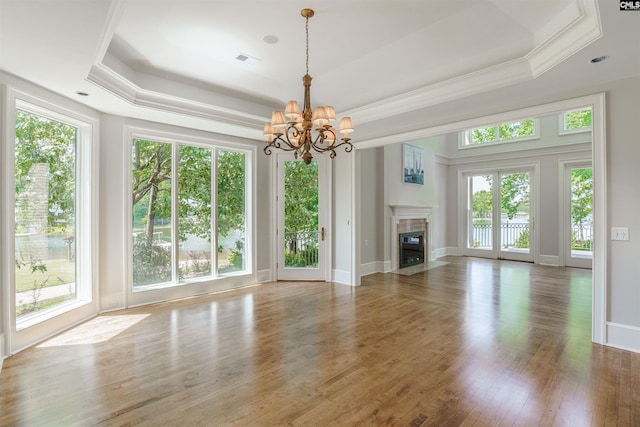 unfurnished living room featuring visible vents, a chandelier, a tray ceiling, and a healthy amount of sunlight
