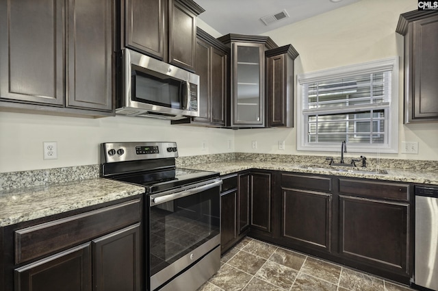 kitchen with visible vents, dark brown cabinetry, light stone counters, a sink, and stainless steel appliances