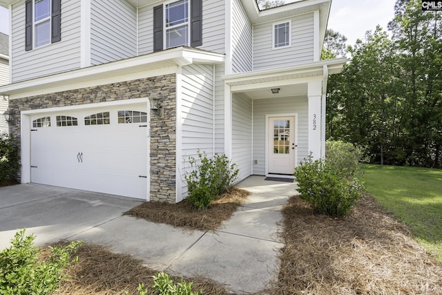entrance to property featuring an attached garage, driveway, and stone siding