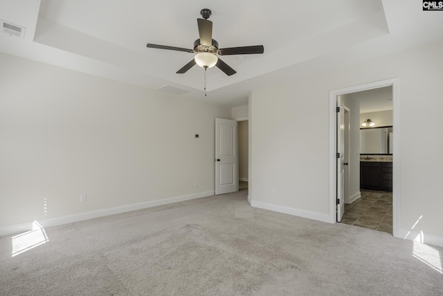 unfurnished bedroom with baseboards, visible vents, light carpet, and a tray ceiling