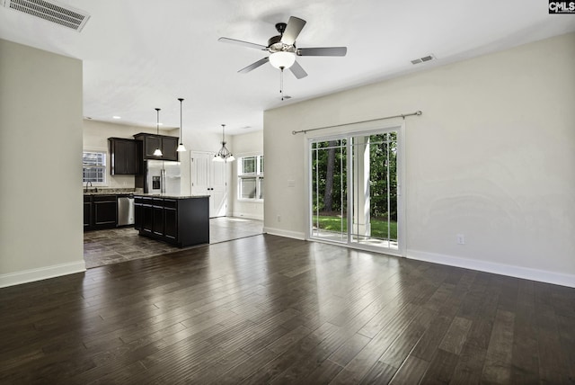 unfurnished living room featuring baseboards, ceiling fan with notable chandelier, dark wood-type flooring, and visible vents