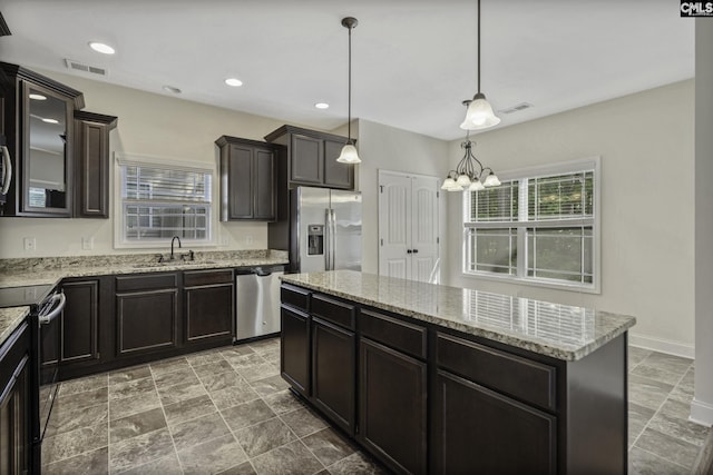 kitchen with a sink, appliances with stainless steel finishes, light stone counters, and visible vents