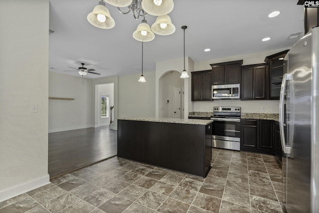 kitchen with appliances with stainless steel finishes, baseboards, a kitchen island, and stone finish flooring