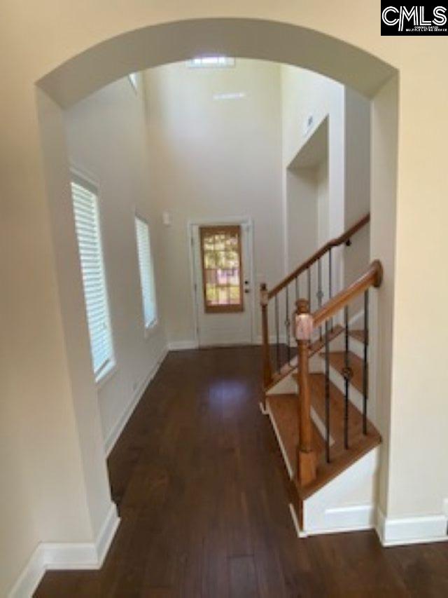 entryway featuring stairs, arched walkways, baseboards, and wood finished floors