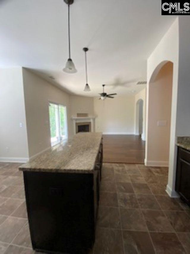 kitchen featuring a fireplace, open floor plan, ceiling fan, decorative light fixtures, and arched walkways