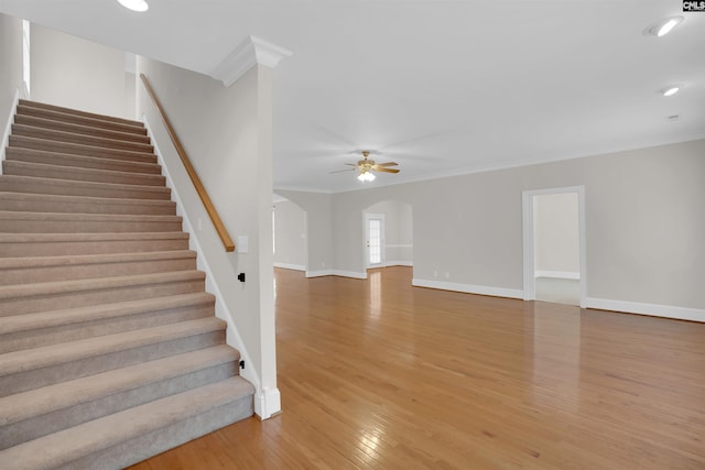 staircase with ornamental molding, wood finished floors, baseboards, ceiling fan, and arched walkways