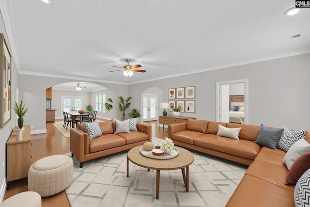 living area featuring ceiling fan, arched walkways, light wood-type flooring, visible vents, and ornamental molding