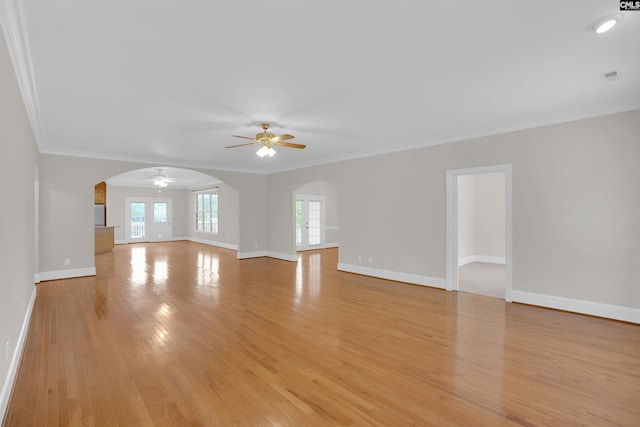 unfurnished living room featuring arched walkways, a ceiling fan, ornamental molding, and light wood-type flooring