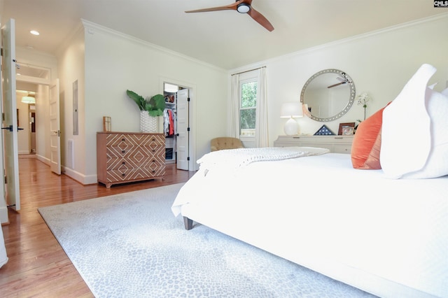 bedroom with a spacious closet, ornamental molding, wood finished floors, and a closet