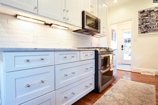 kitchen featuring appliances with stainless steel finishes, white cabinetry, backsplash, visible vents, and dark wood-style floors