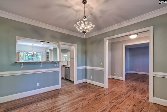 unfurnished dining area featuring crown molding, a sink, a chandelier, baseboards, and wood finished floors