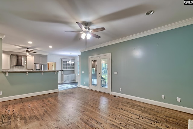 unfurnished living room with crown molding, baseboards, ceiling fan with notable chandelier, and wood finished floors