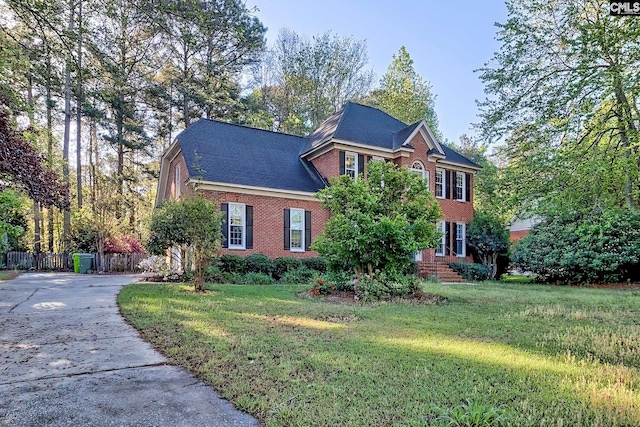 colonial house featuring brick siding, a front lawn, fence, and driveway