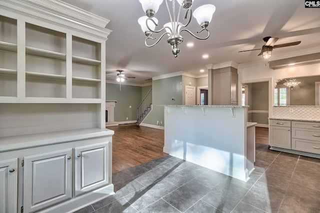 kitchen with light stone countertops, hanging light fixtures, ceiling fan with notable chandelier, dark tile patterned floors, and ornamental molding