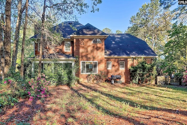 back of property with fence, a shingled roof, a lawn, and brick siding