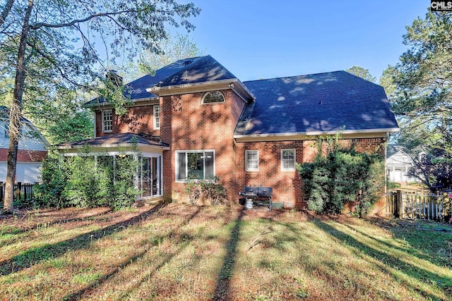 rear view of house with a lawn, brick siding, fence, and a shingled roof