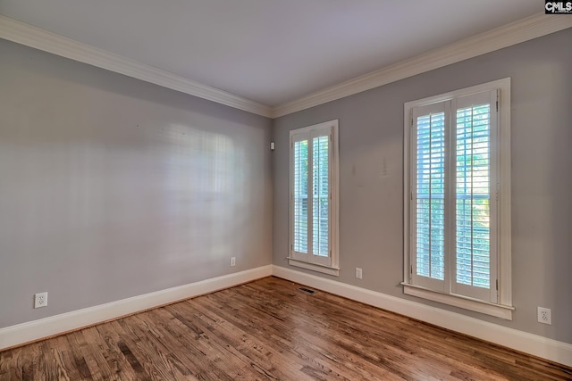 spare room featuring baseboards, visible vents, ornamental molding, and wood finished floors