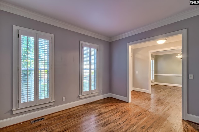 unfurnished room featuring visible vents, wood finished floors, baseboards, a chandelier, and ornamental molding