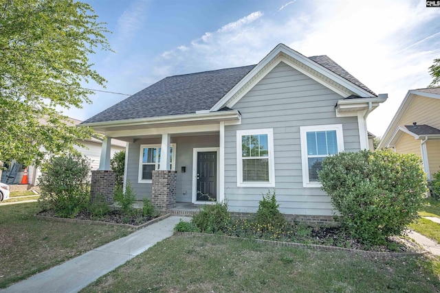 view of front of house with a porch, a shingled roof, and a front yard