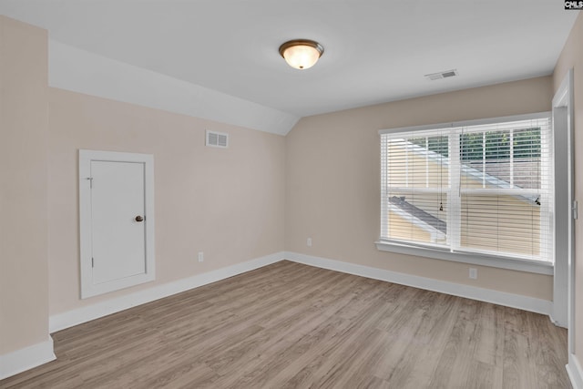 empty room with visible vents, light wood-style floors, and vaulted ceiling