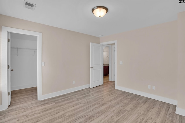 unfurnished bedroom featuring baseboards, a walk in closet, and light wood-type flooring
