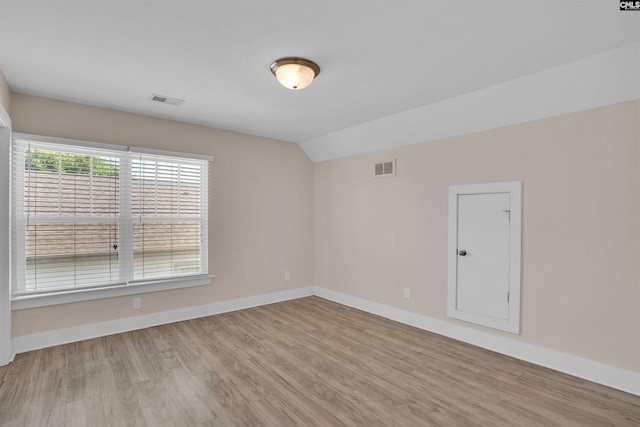 spare room with baseboards, visible vents, wood finished floors, and vaulted ceiling