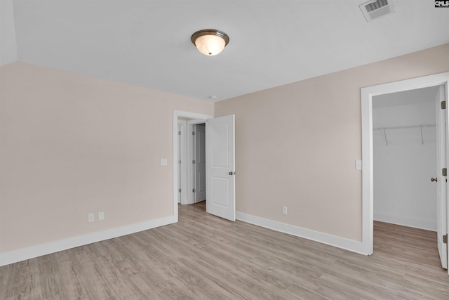 unfurnished bedroom featuring baseboards, visible vents, a spacious closet, and light wood finished floors