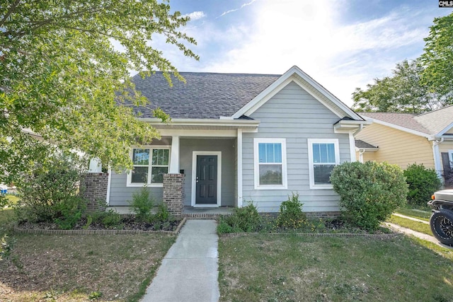view of front of property featuring a porch, a shingled roof, and a front yard