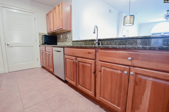kitchen featuring brown cabinetry, backsplash, dishwasher, light tile patterned floors, and dark stone counters