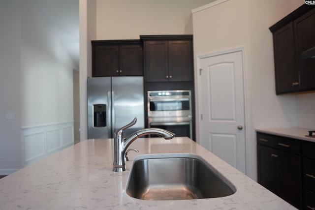 509 Malachite Ln, Chapin, SC 29036 - kitchen featuring wainscoting, dark brown cabinetry, light stone counters, a sink, and stainless steel appliances