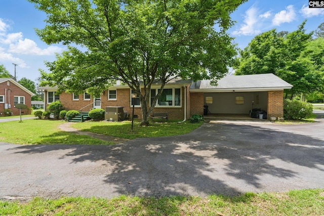 view of front of home with brick siding, aphalt driveway, a front yard, central AC unit, and a carport