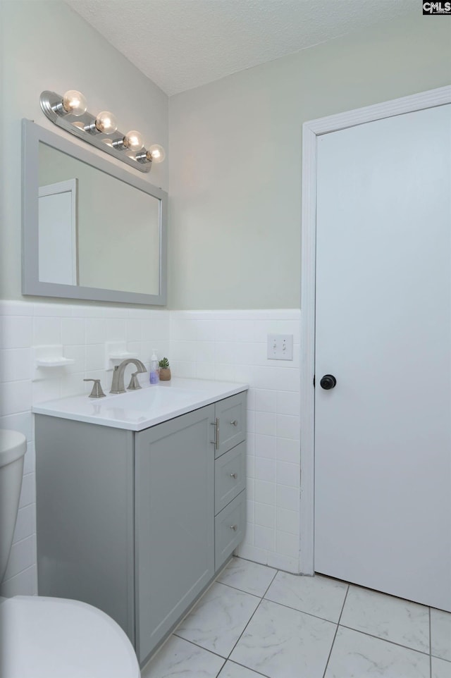 bathroom with wainscoting, vanity, toilet, marble finish floor, and tile walls