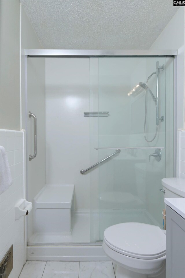 full bathroom with toilet, a textured ceiling, marble finish floor, and a stall shower