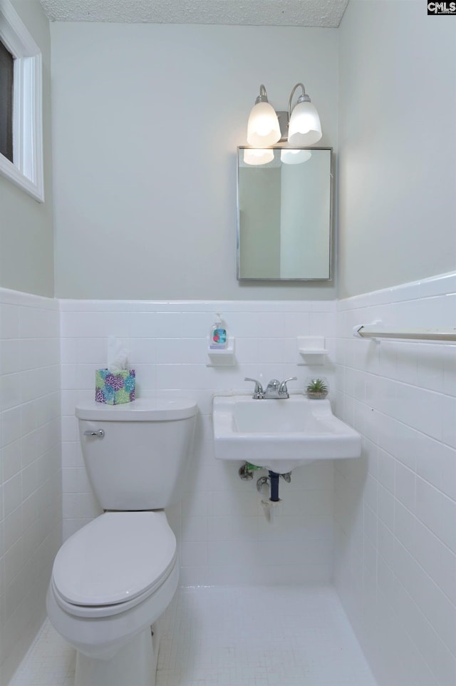 bathroom with a sink, a wainscoted wall, toilet, and tile walls