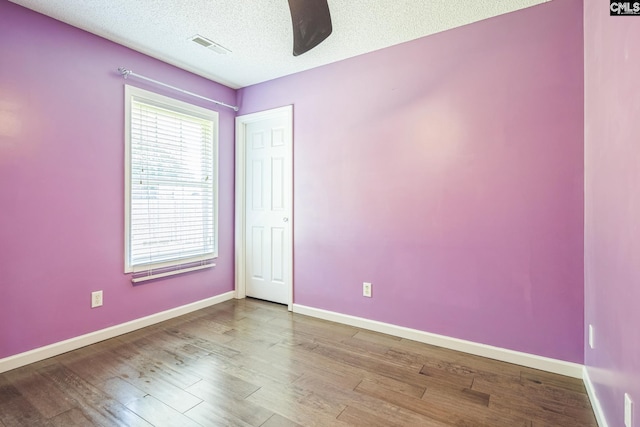 empty room with a textured ceiling, baseboards, visible vents, and wood finished floors