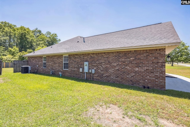 view of side of home featuring central air condition unit, a lawn, a shingled roof, and brick siding