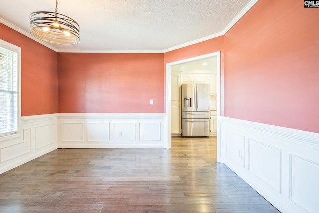 empty room with wood finished floors, ornamental molding, a wainscoted wall, and a chandelier