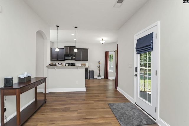 kitchen featuring dark wood-style flooring, a peninsula, black microwave, baseboards, and arched walkways