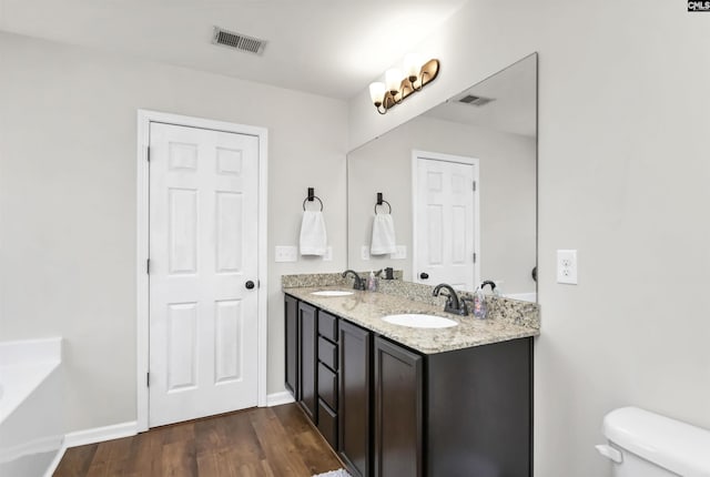 bathroom featuring a sink, toilet, wood finished floors, and visible vents