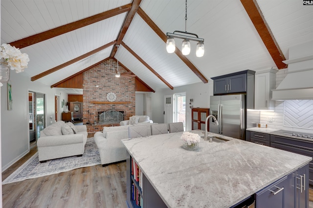 kitchen with light stone countertops, black electric stovetop, stainless steel fridge with ice dispenser, a brick fireplace, and wood finished floors
