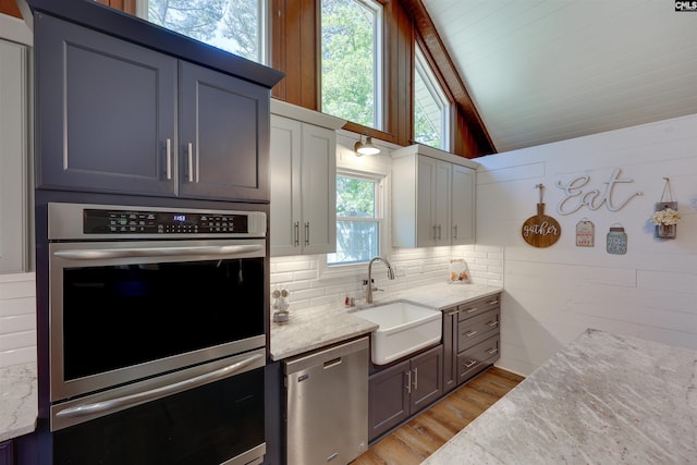 kitchen featuring a sink, light stone counters, light wood finished floors, lofted ceiling, and stainless steel appliances
