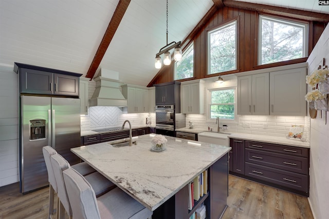 kitchen featuring a sink, premium range hood, light stone countertops, and stainless steel appliances