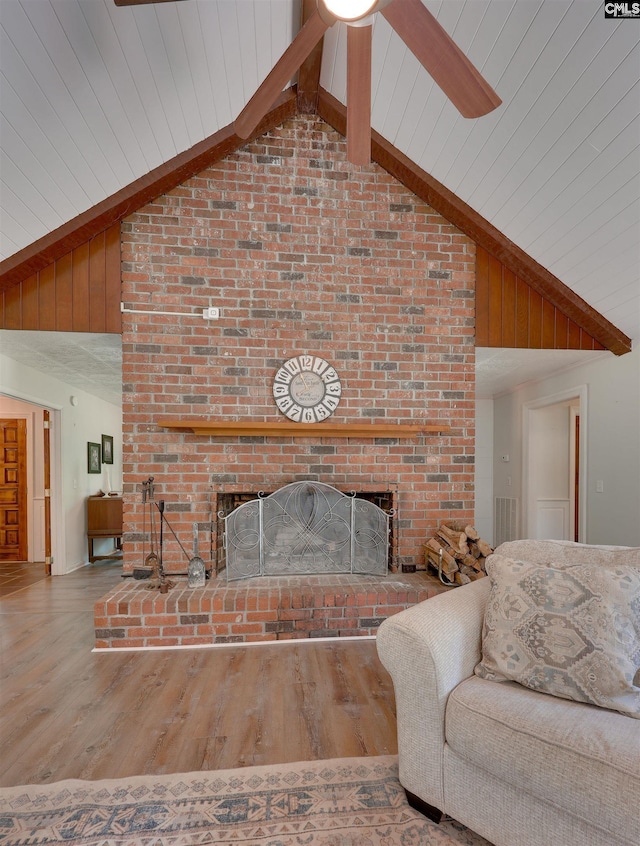 living area featuring high vaulted ceiling, a ceiling fan, a brick fireplace, and wood finished floors