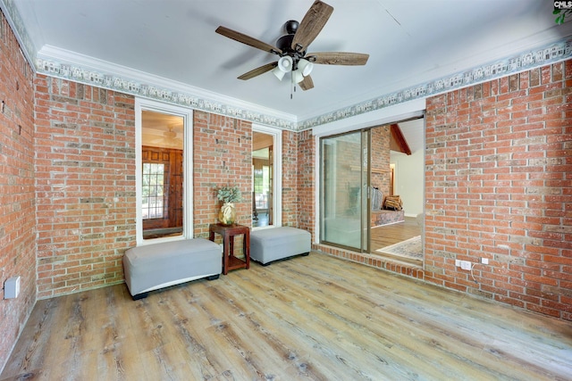 interior space with brick wall, ceiling fan, ornamental molding, and wood finished floors