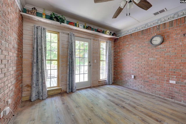 unfurnished room featuring wood finished floors, ceiling fan, brick wall, and visible vents