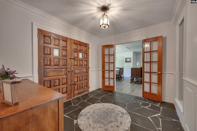 entrance foyer featuring french doors, ornamental molding, a textured ceiling, and wainscoting