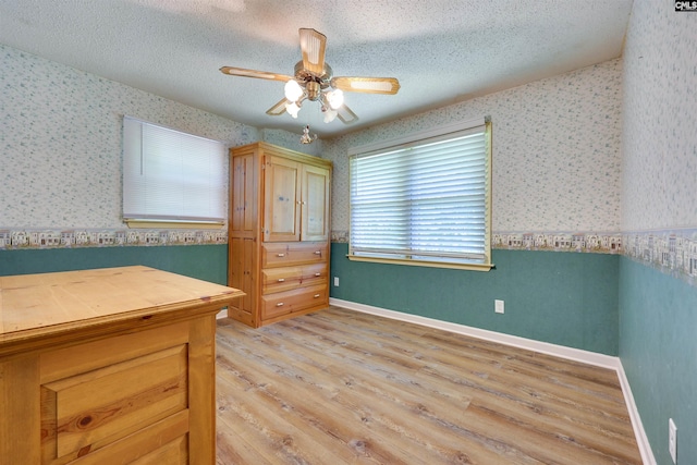 unfurnished bedroom with light wood-style floors, ceiling fan, wallpapered walls, and a textured ceiling