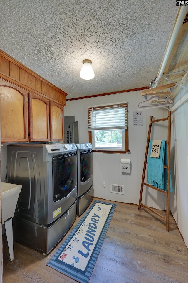 washroom featuring washer and dryer, cabinet space, light wood finished floors, a textured ceiling, and visible vents