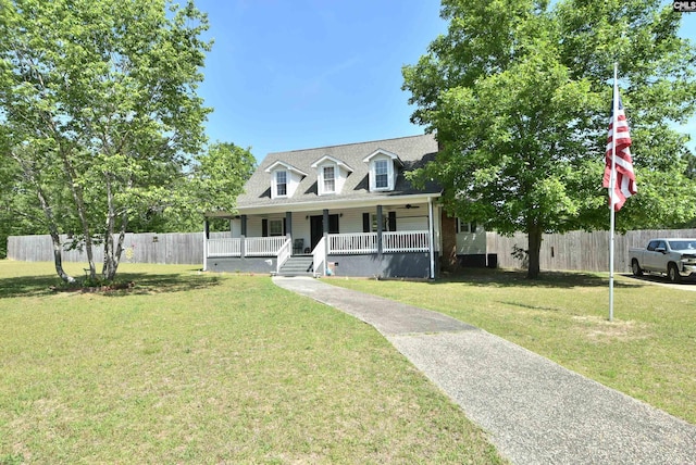 new england style home featuring a porch, roof with shingles, fence, and a front yard